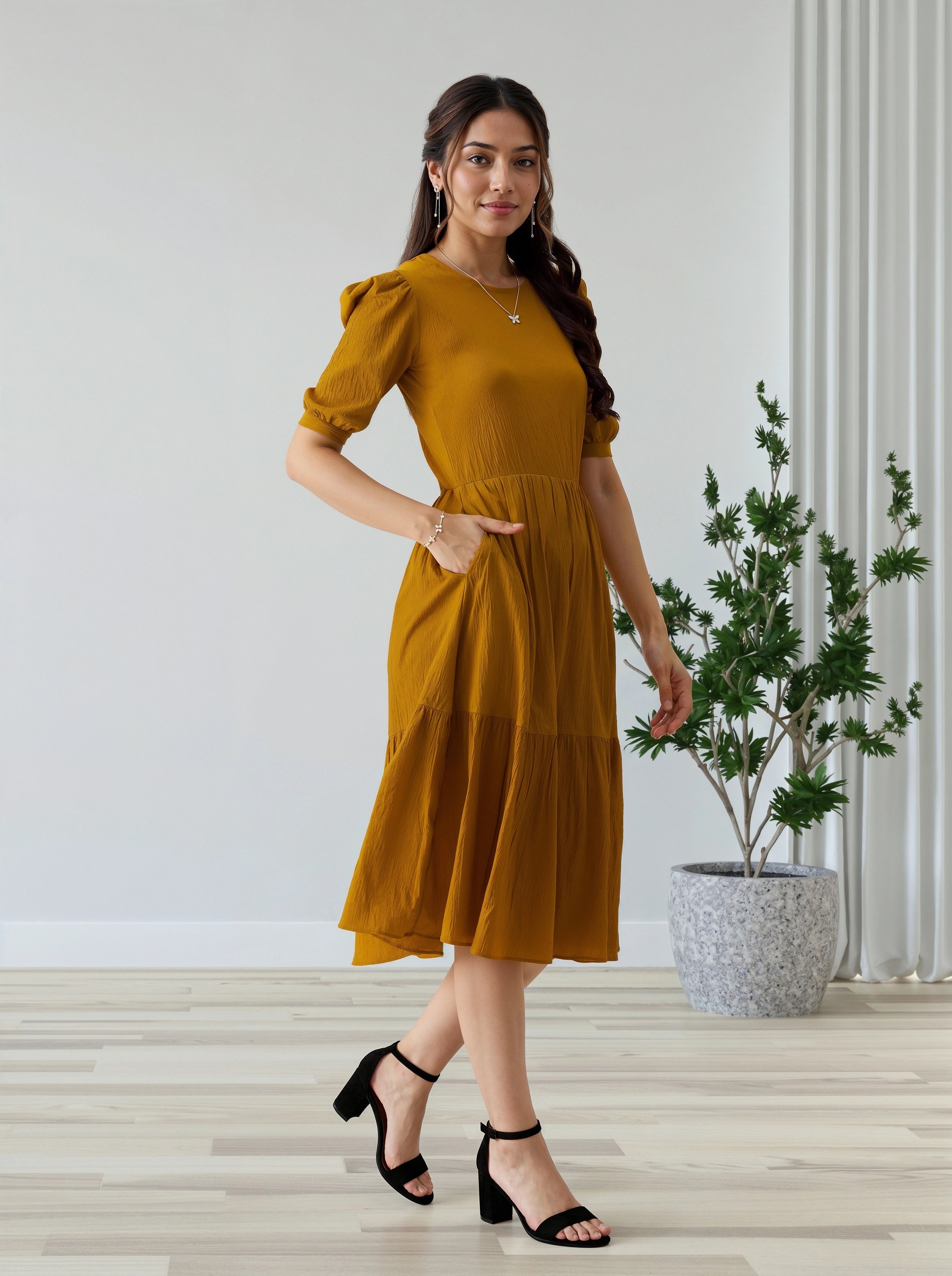 Woman in a mustard yellow dress standing indoors with a plant in the background