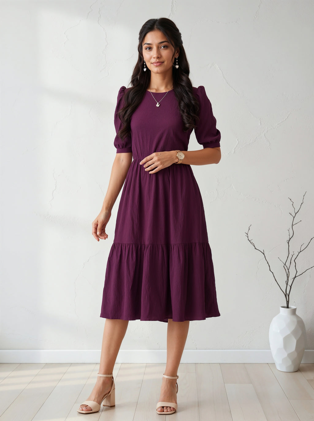 Woman wearing a purple dress standing in a room with a white wall and a vase.