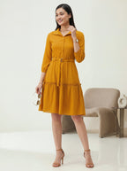 Woman wearing a mustard yellow dress standing in a minimalistic room.