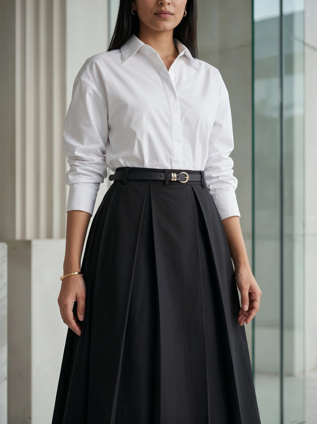 Person wearing a white shirt and black pleated skirt standing indoors.