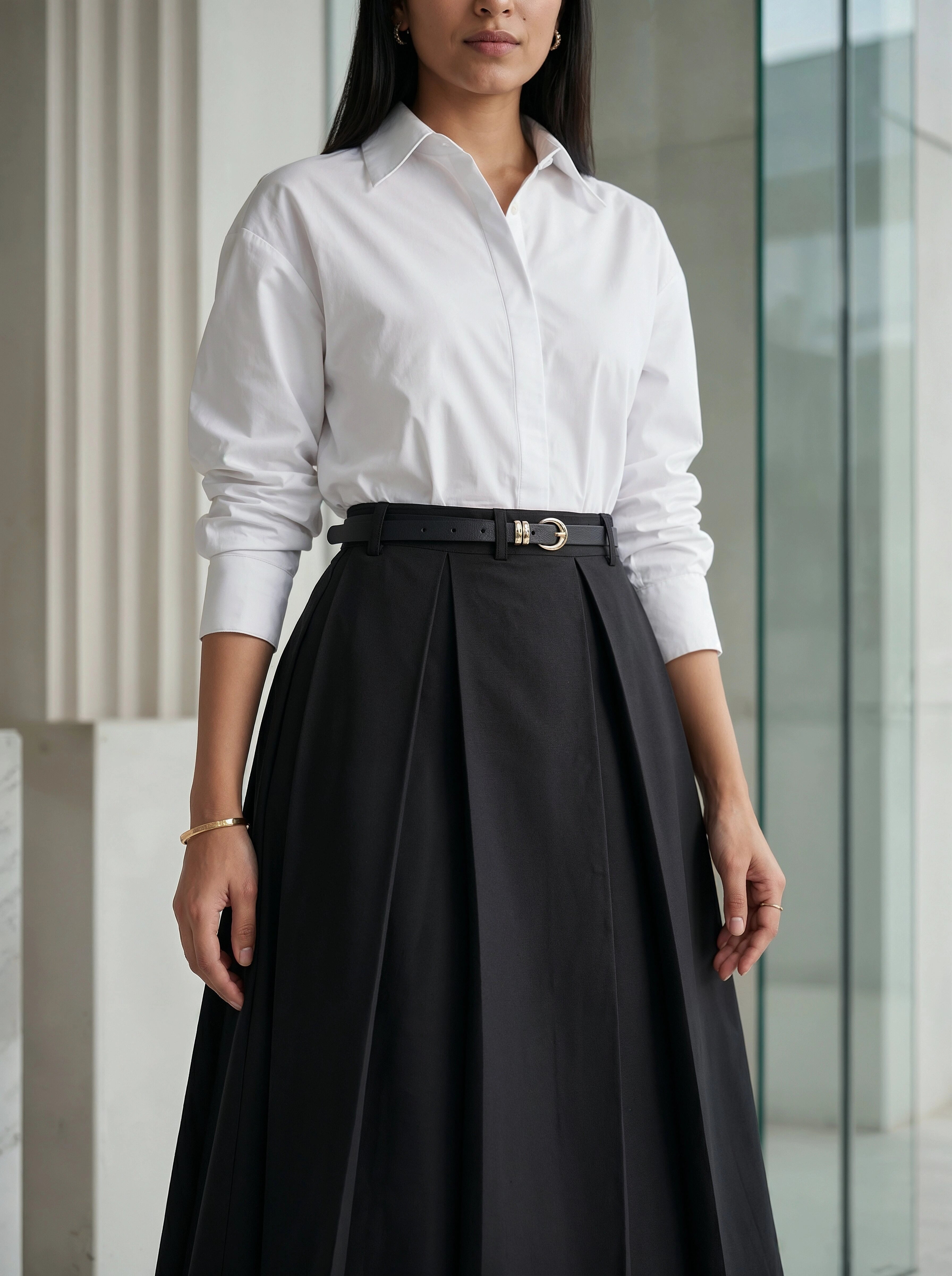 Person wearing a white shirt and black pleated skirt standing indoors.
