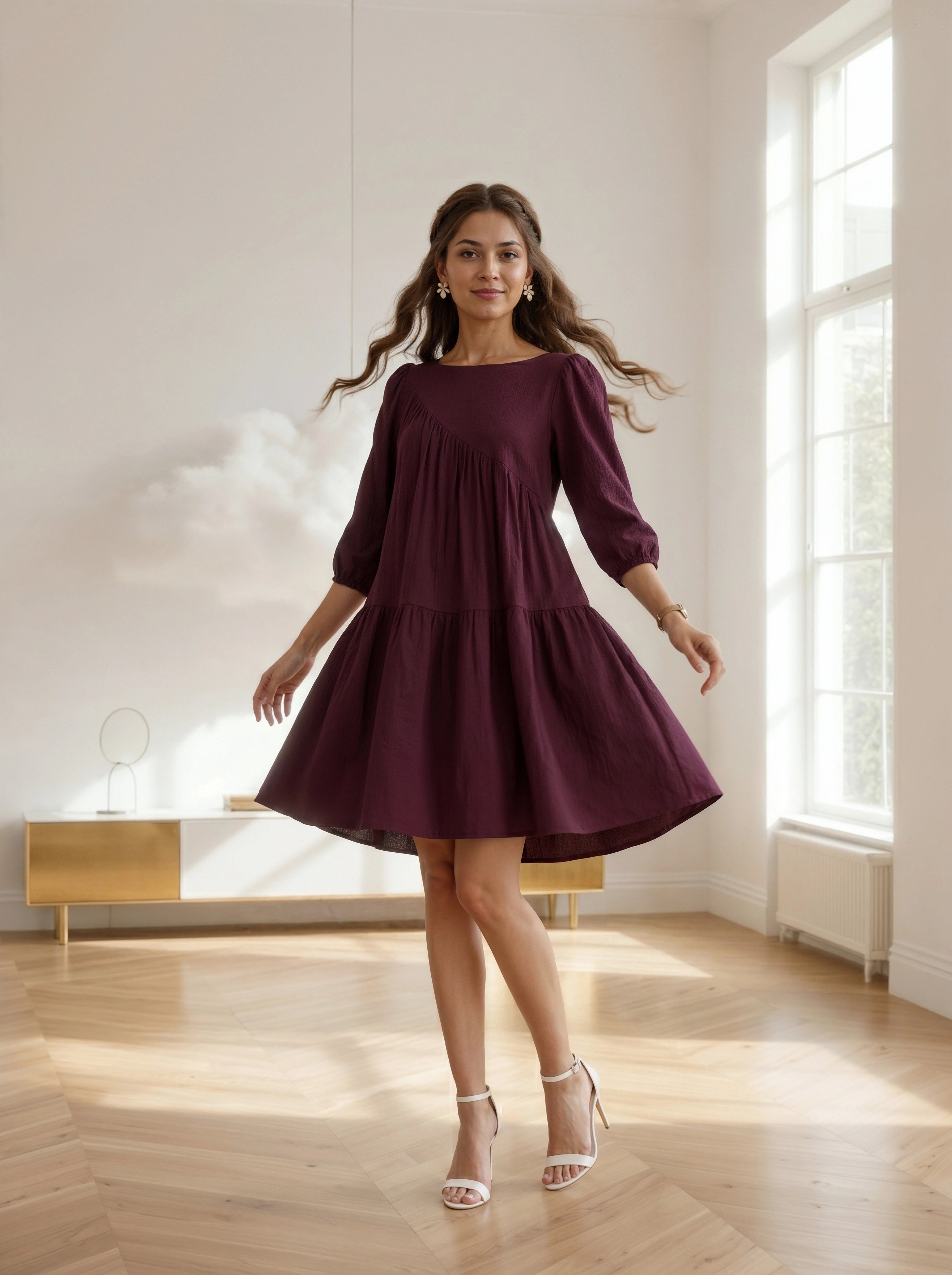 Woman in a burgundy dress standing in a bright room with large windows.