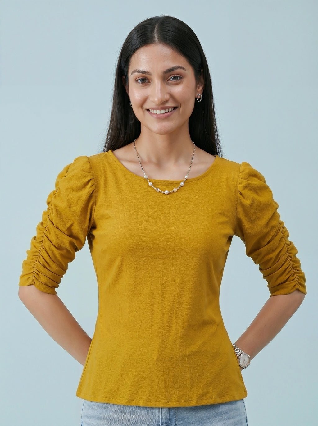 Woman wearing a mustard yellow long-sleeve top against a light blue background