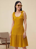 Woman wearing a mustard yellow dress with ruffled straps against a beige background