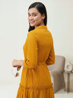 Woman in a mustard yellow dress holding sunglasses indoors.