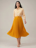 Woman wearing a yellow pleated skirt and patterned blouse on a plain background