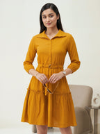 Woman wearing a mustard yellow dress in a minimal indoor setting