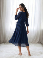 Woman wearing a blue dress standing in front of white curtains