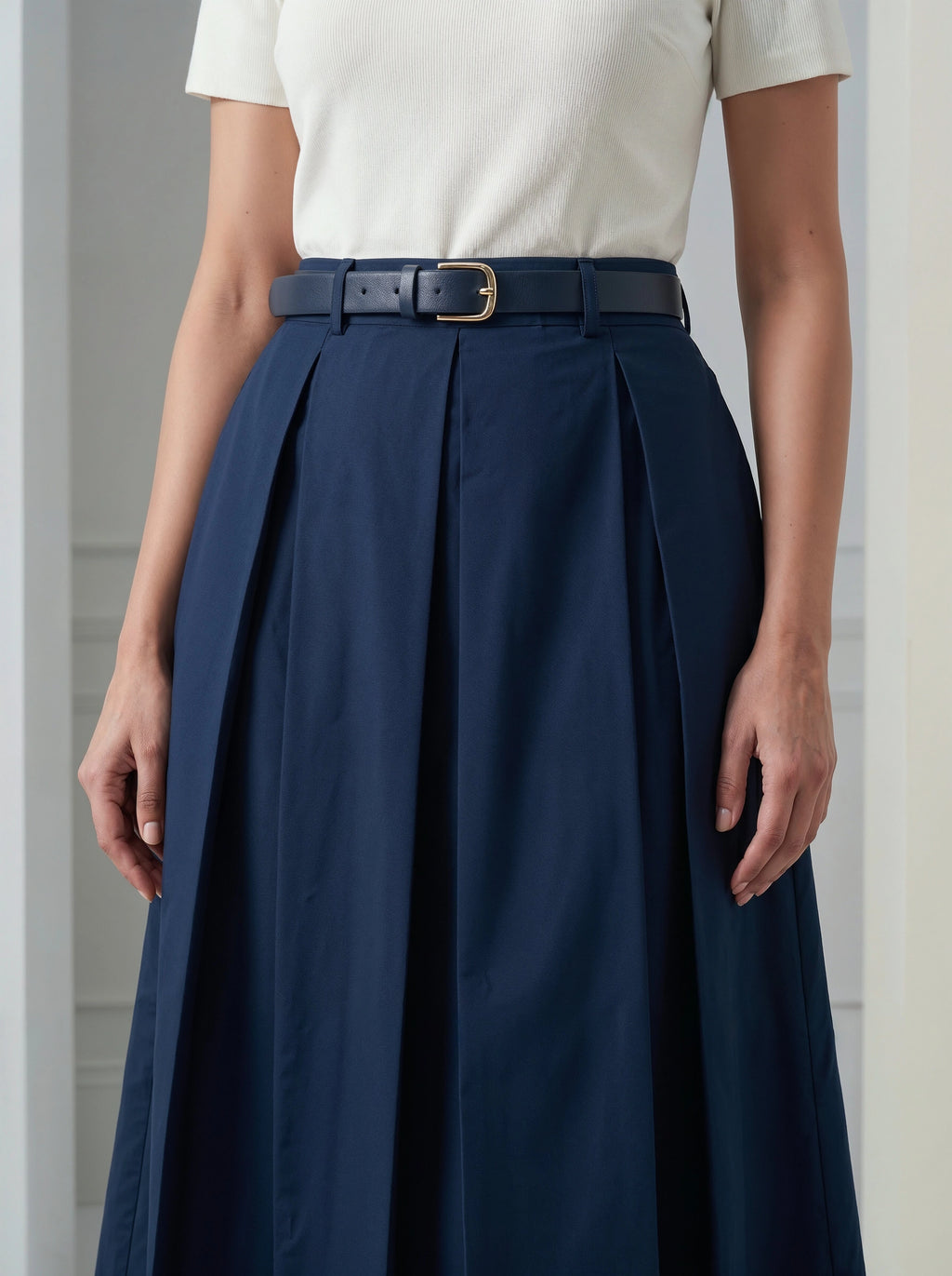 Person wearing a navy pleated skirt with a white top against a neutral background