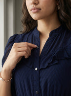 Woman wearing a Navy dress with ruffled details standing against a white wall.