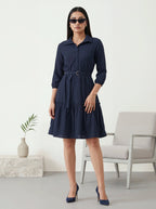 Woman wearing a navy blue dress in a minimalistic room.