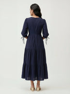 Woman wearing a navy blue dress with tiered skirt on a white background