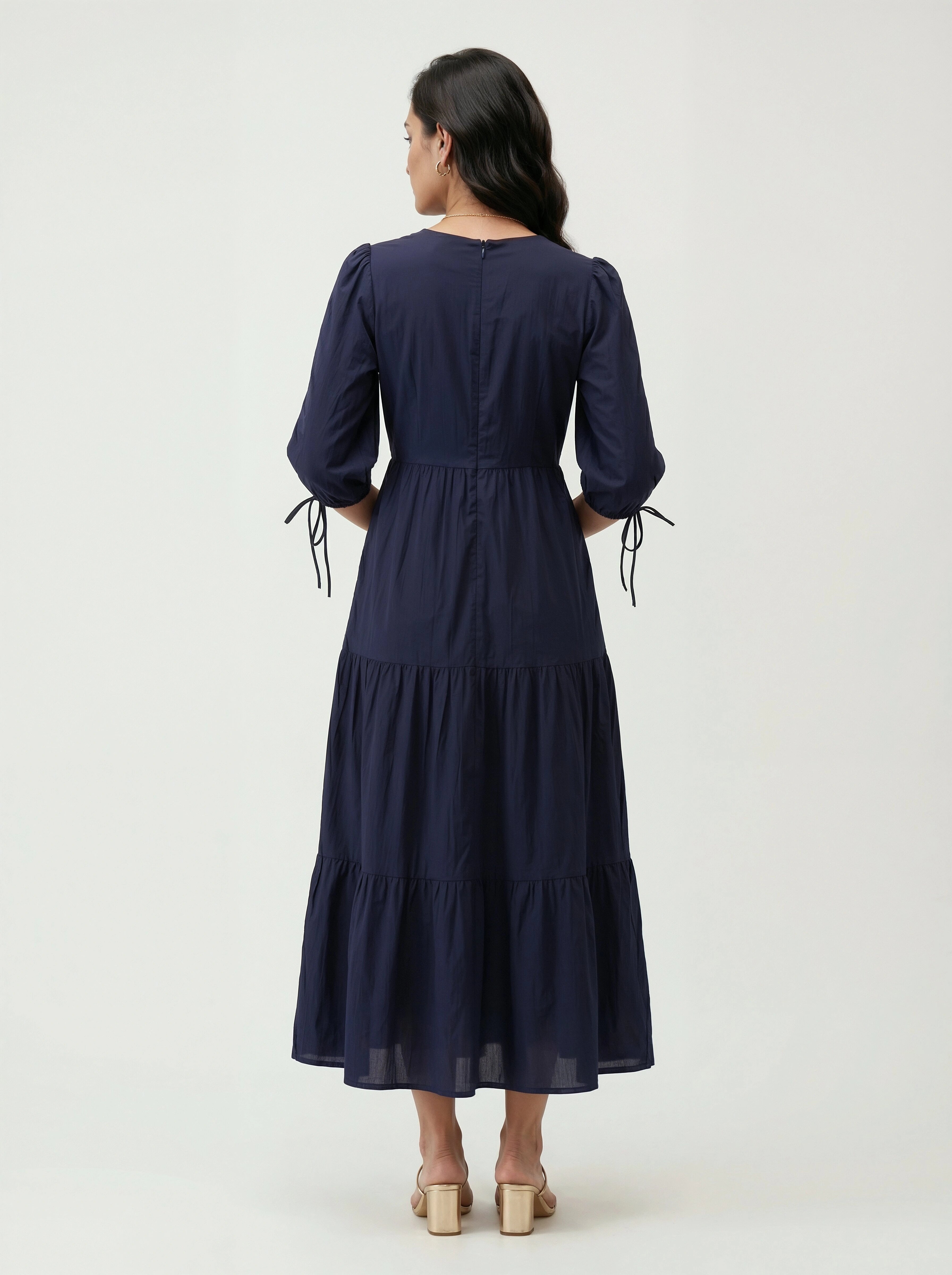 Woman wearing a navy blue dress with tiered skirt on a white background