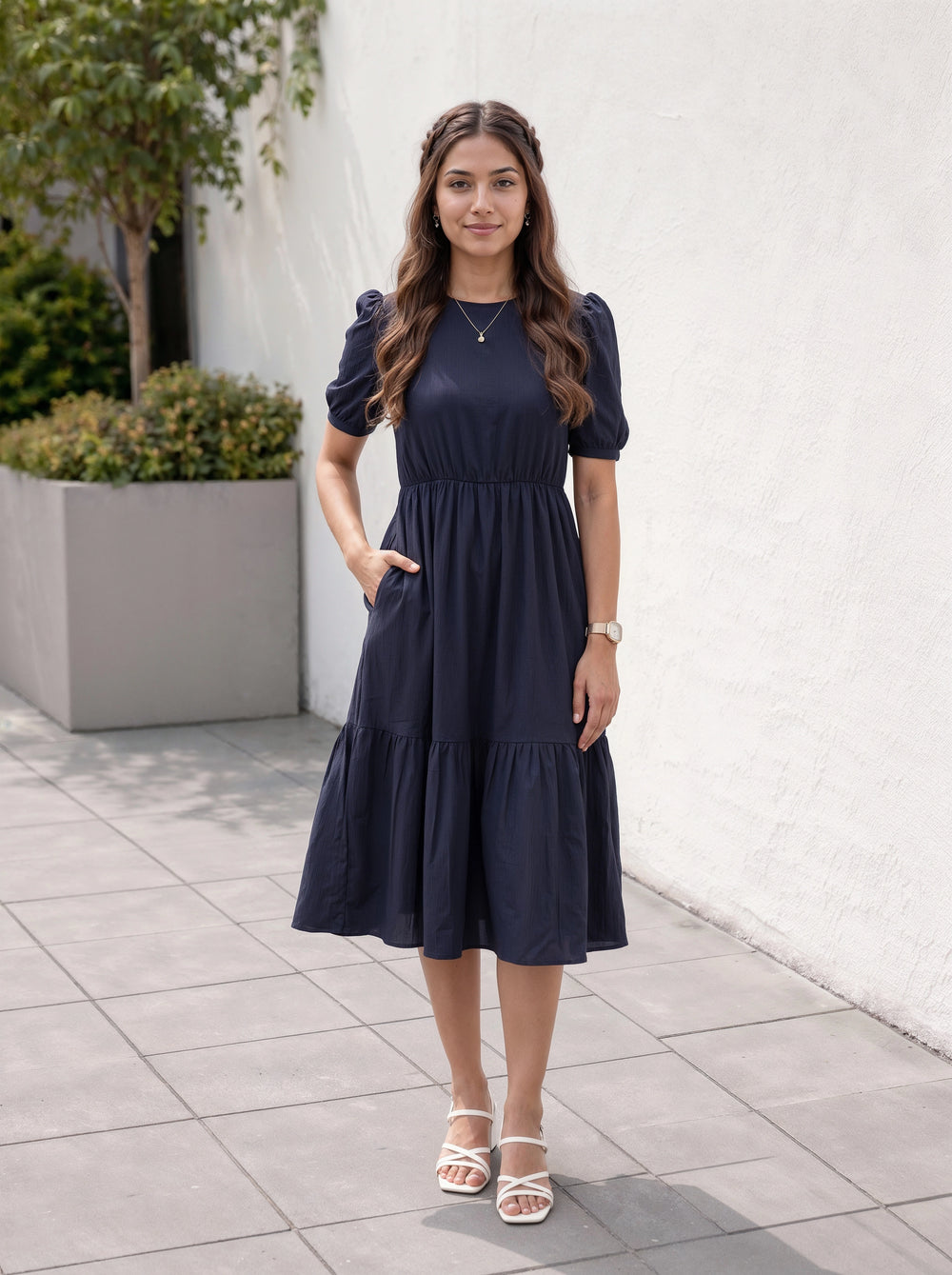 Woman wearing a navy blue dress standing outdoors on a tiled pavement.