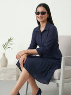 Woman in a navy dress sitting on a chair with a white background