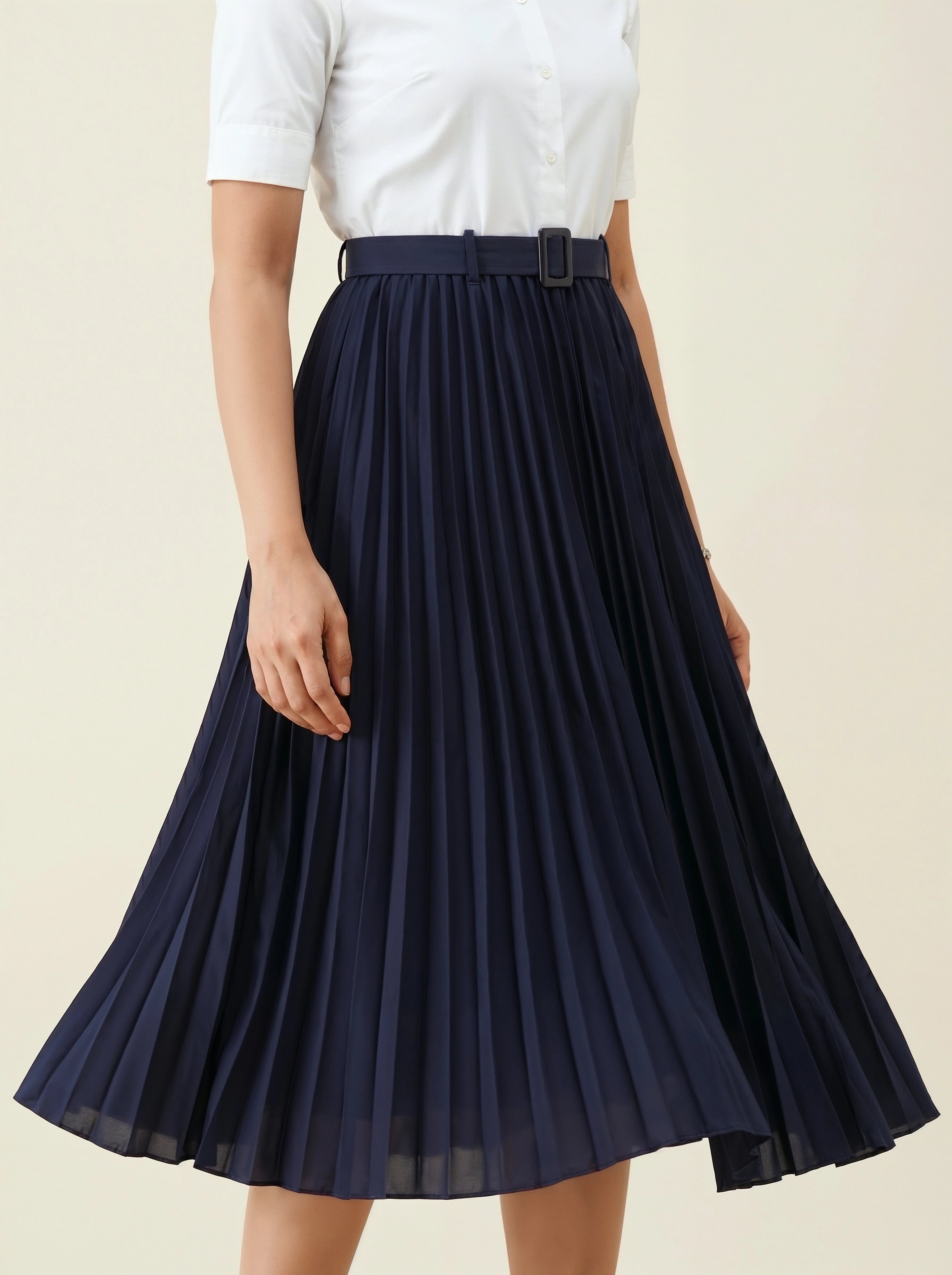 Navy pleated skirt worn with a white top on a beige background