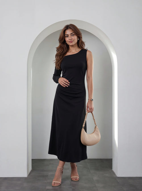 A woman modeling a black long-sleeve midi dress with a draped neckline, standing in front of a white arched wall and holding a beige crescent handbag.