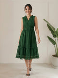 Woman wearing a green dress standing in a minimalistic room with a plant.