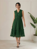 Woman wearing a green dress standing in a minimalistic room with a plant.