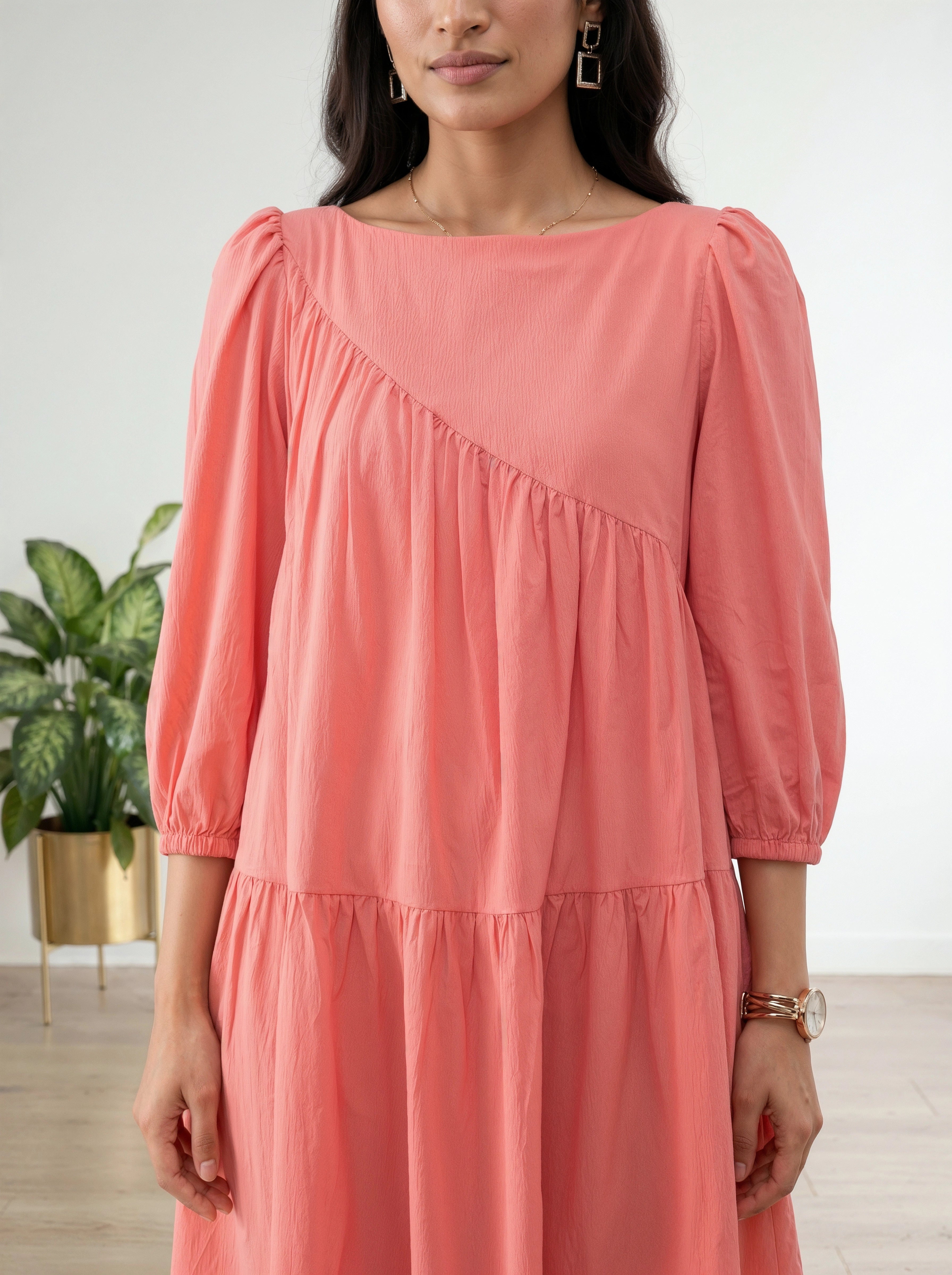 Woman wearing a coral dress with a plant in the background