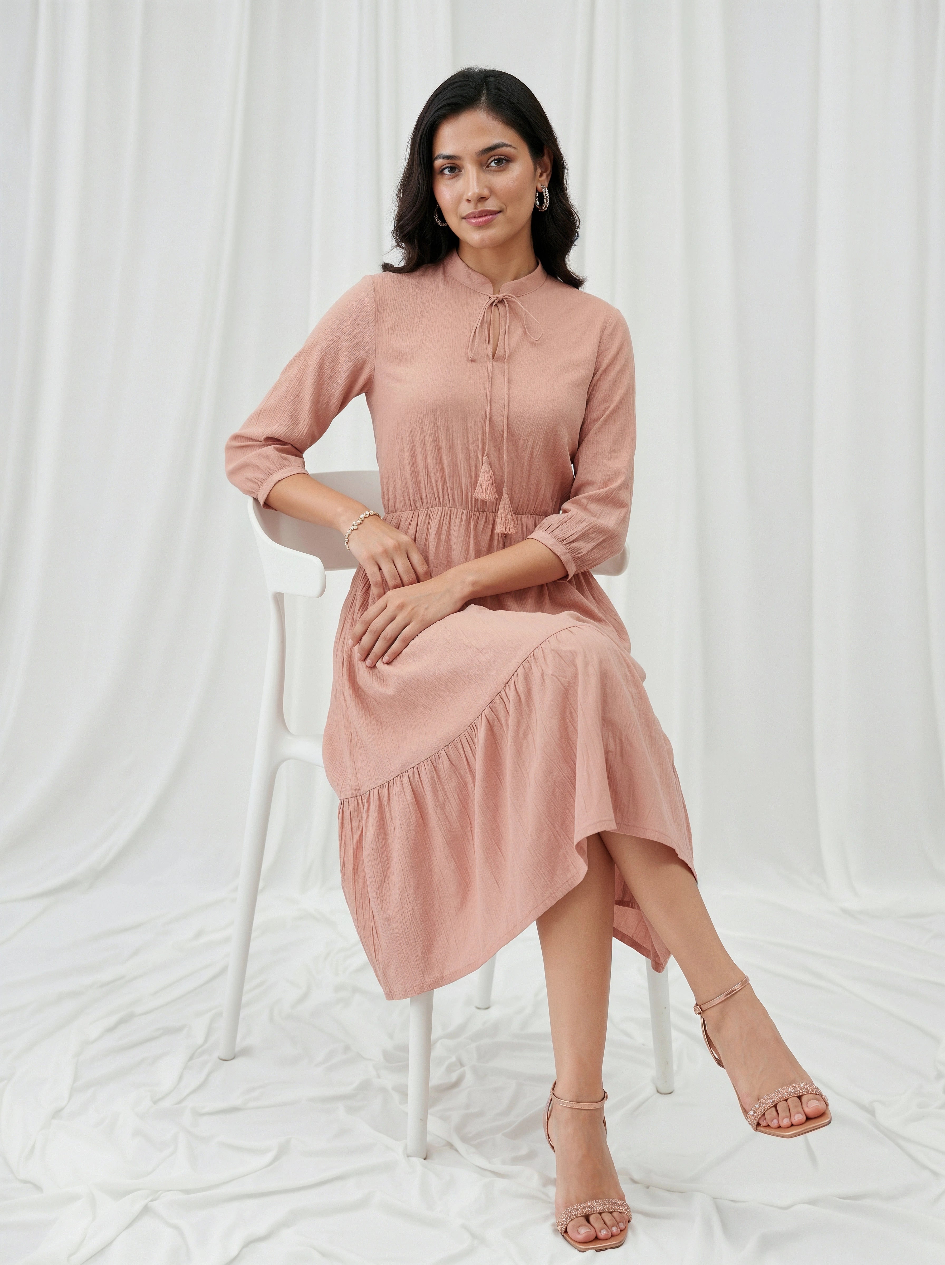 Woman in a pink dress sitting on a white stool against a white curtain background