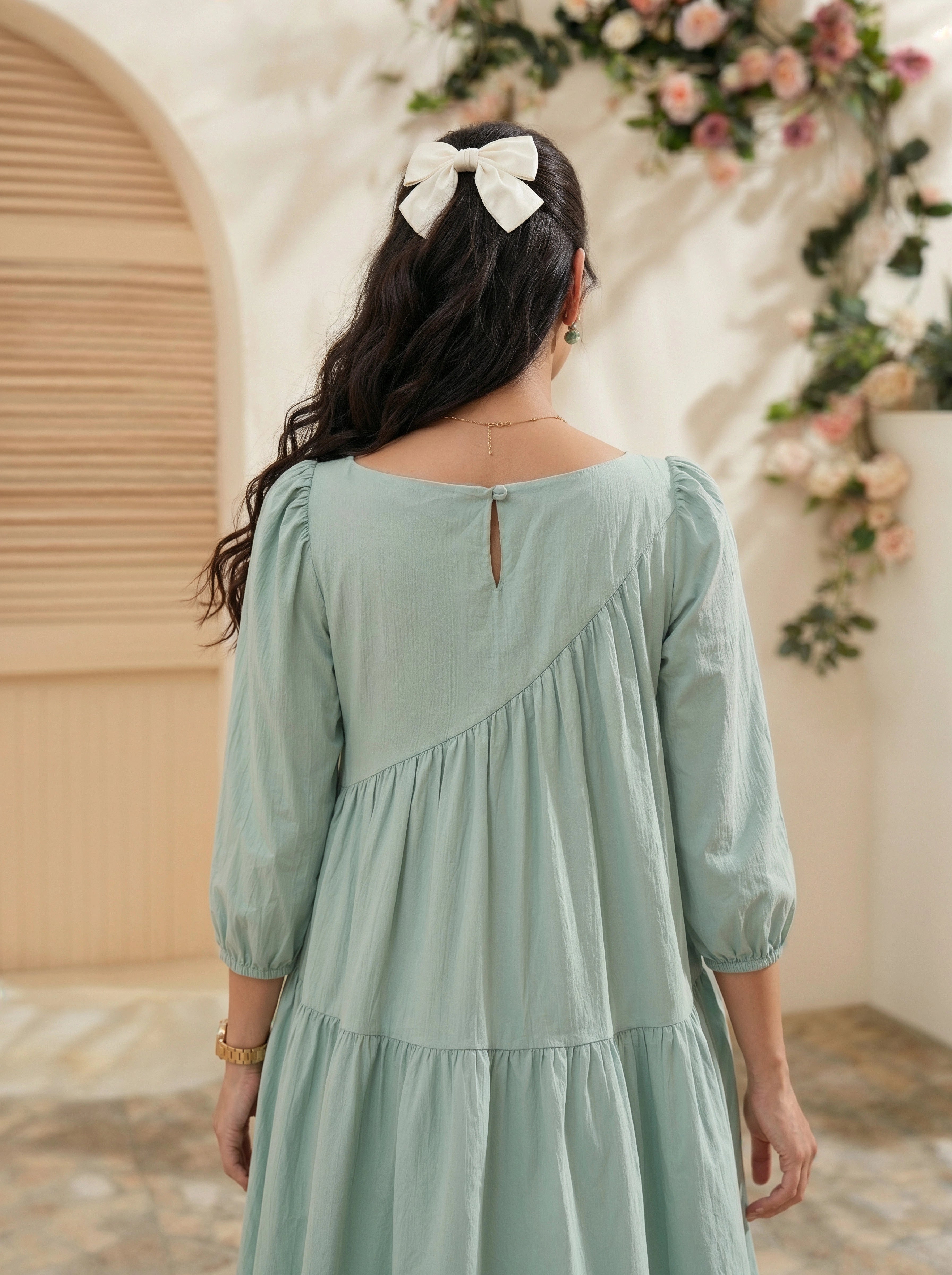 Woman wearing a light green dress with a floral backdrop