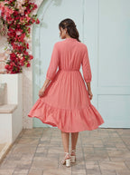 Woman wearing a pink dress standing in front of a decorative floral wall.