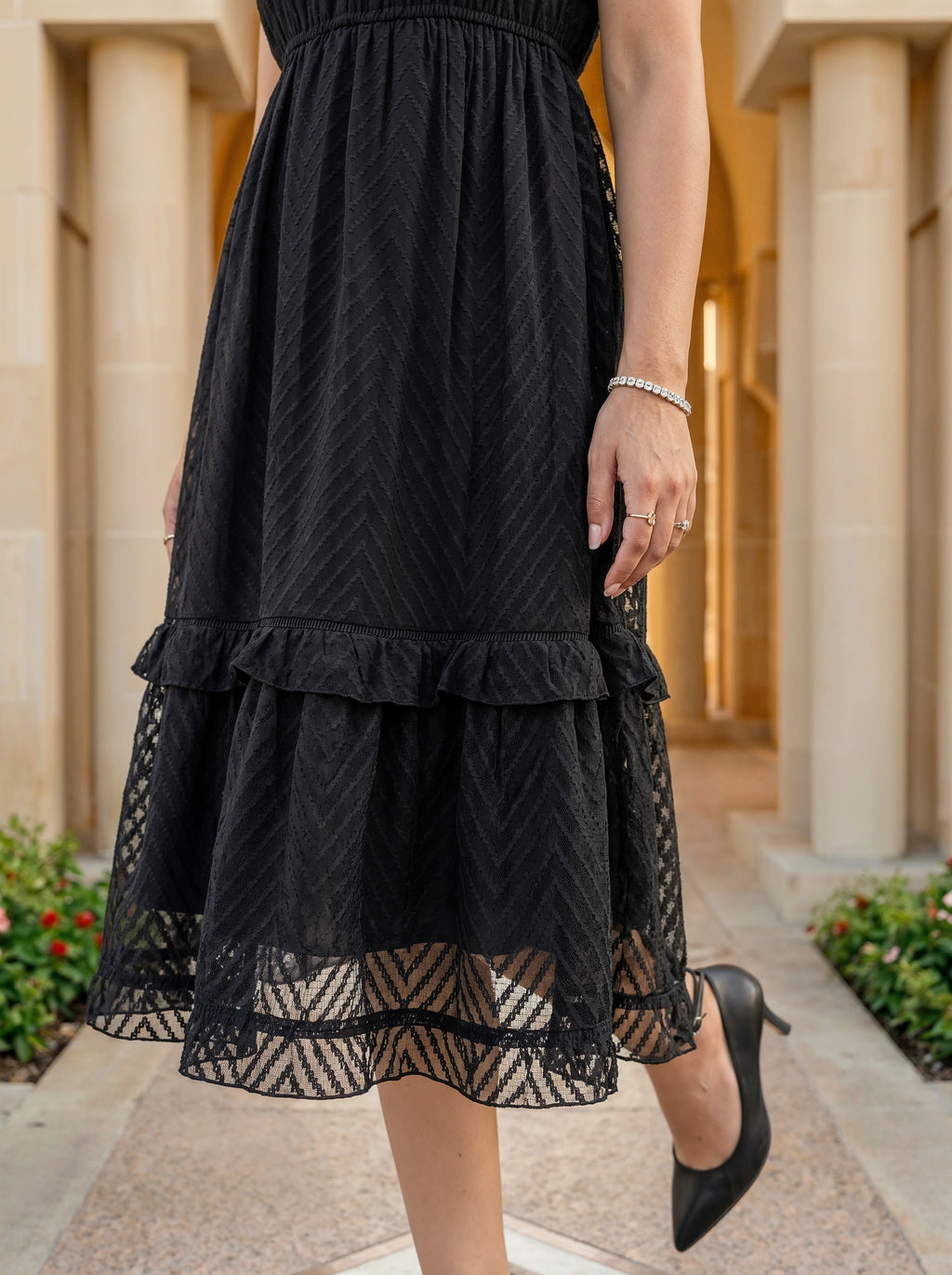 Black lace dress worn by a person in an outdoor setting with columns and plants.