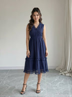 Woman wearing a navy blue lace dress standing in a room with light gray floor and white walls.