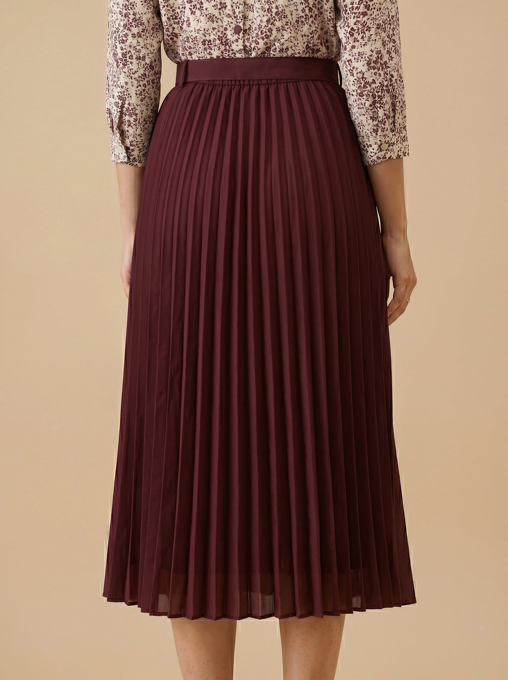 Person wearing a pleated burgundy skirt and patterned blouse on a beige background