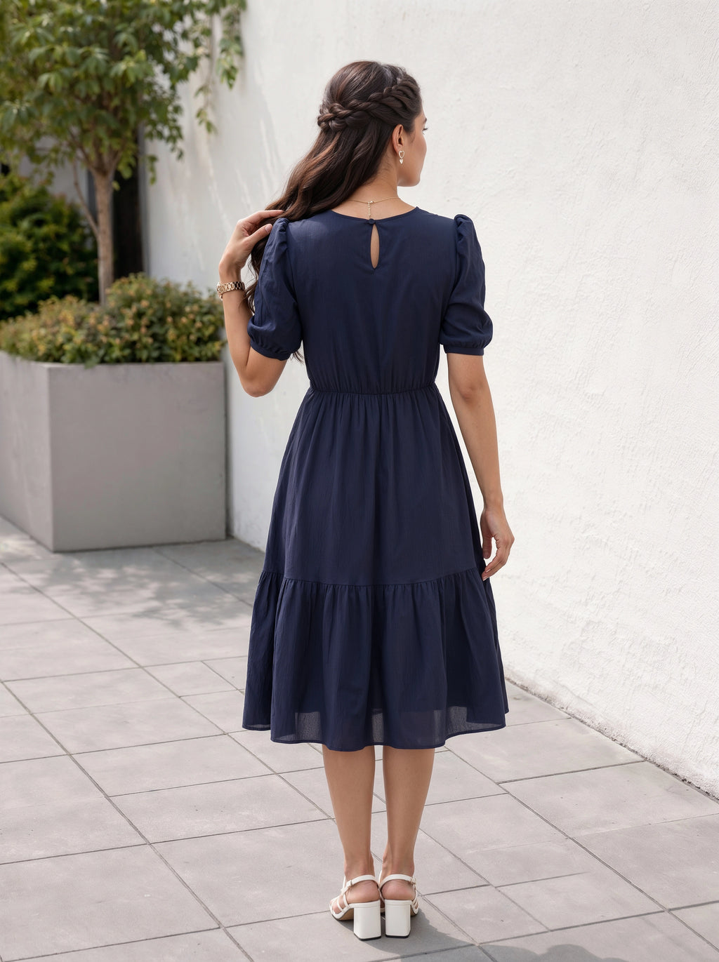 Woman wearing a navy blue dress with puff sleeves, standing on a tiled pavement.