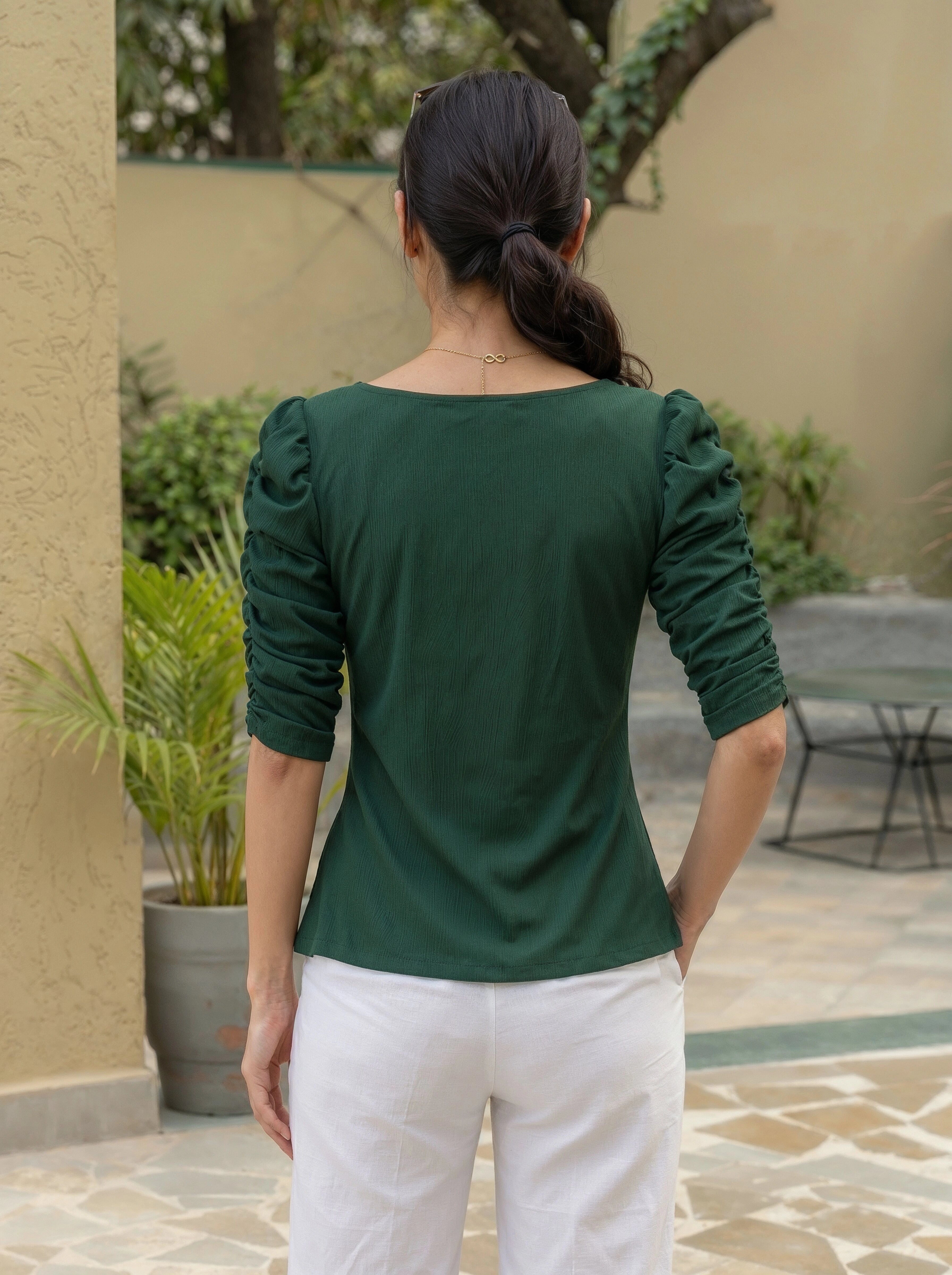 Person wearing a green top with ruffled sleeves in an outdoor setting