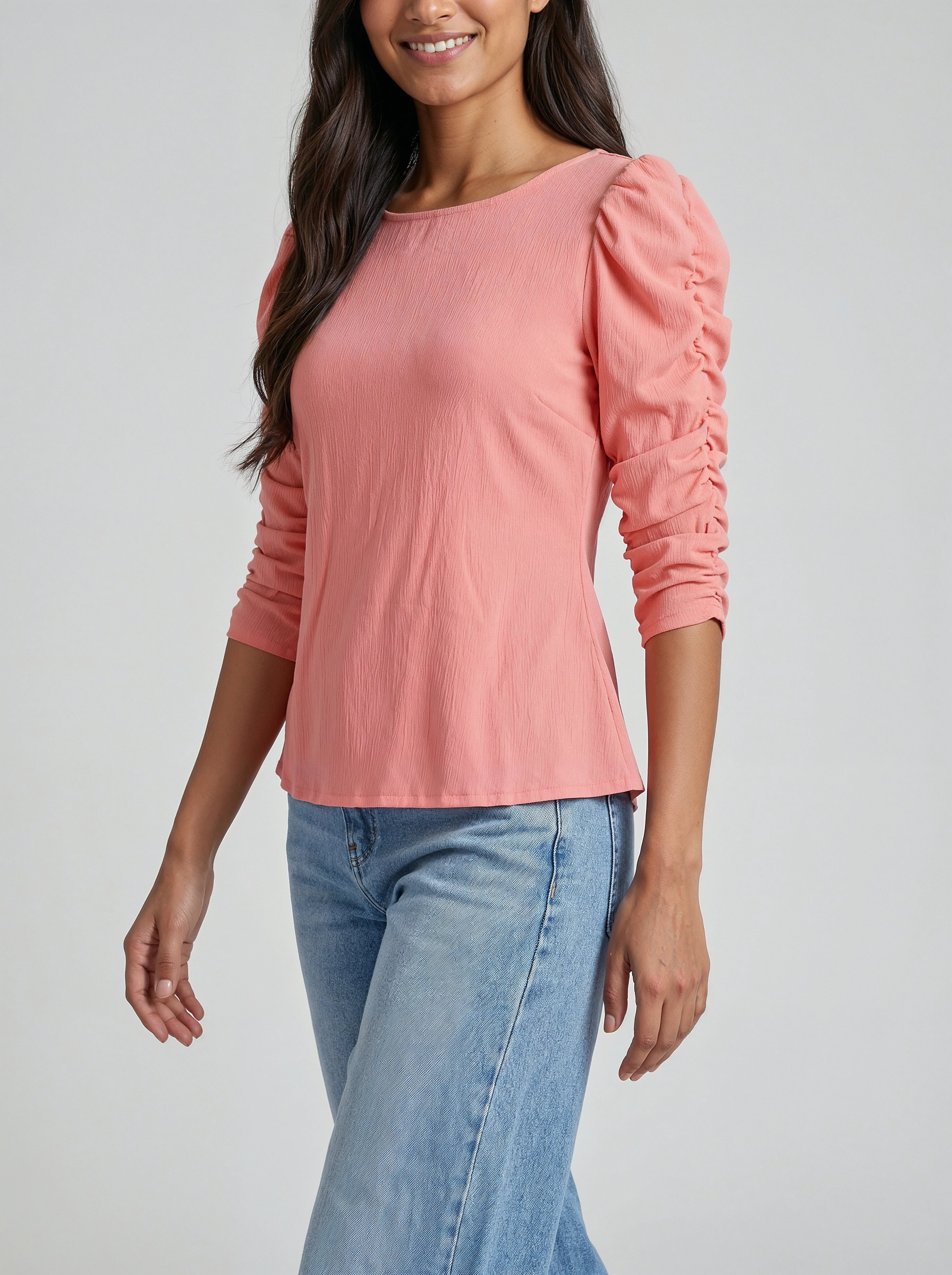 Woman wearing a pink long-sleeve top and blue jeans on a plain background