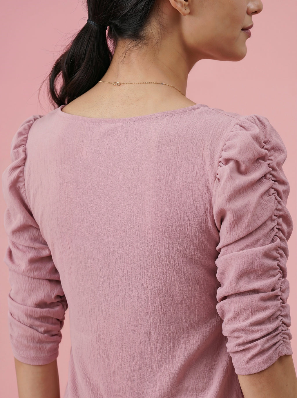 Person wearing a pink long-sleeve top with ruffled sleeves against a pink background