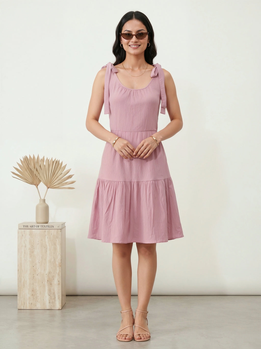 Woman wearing a pink dress standing next to a decorative plant on a white background