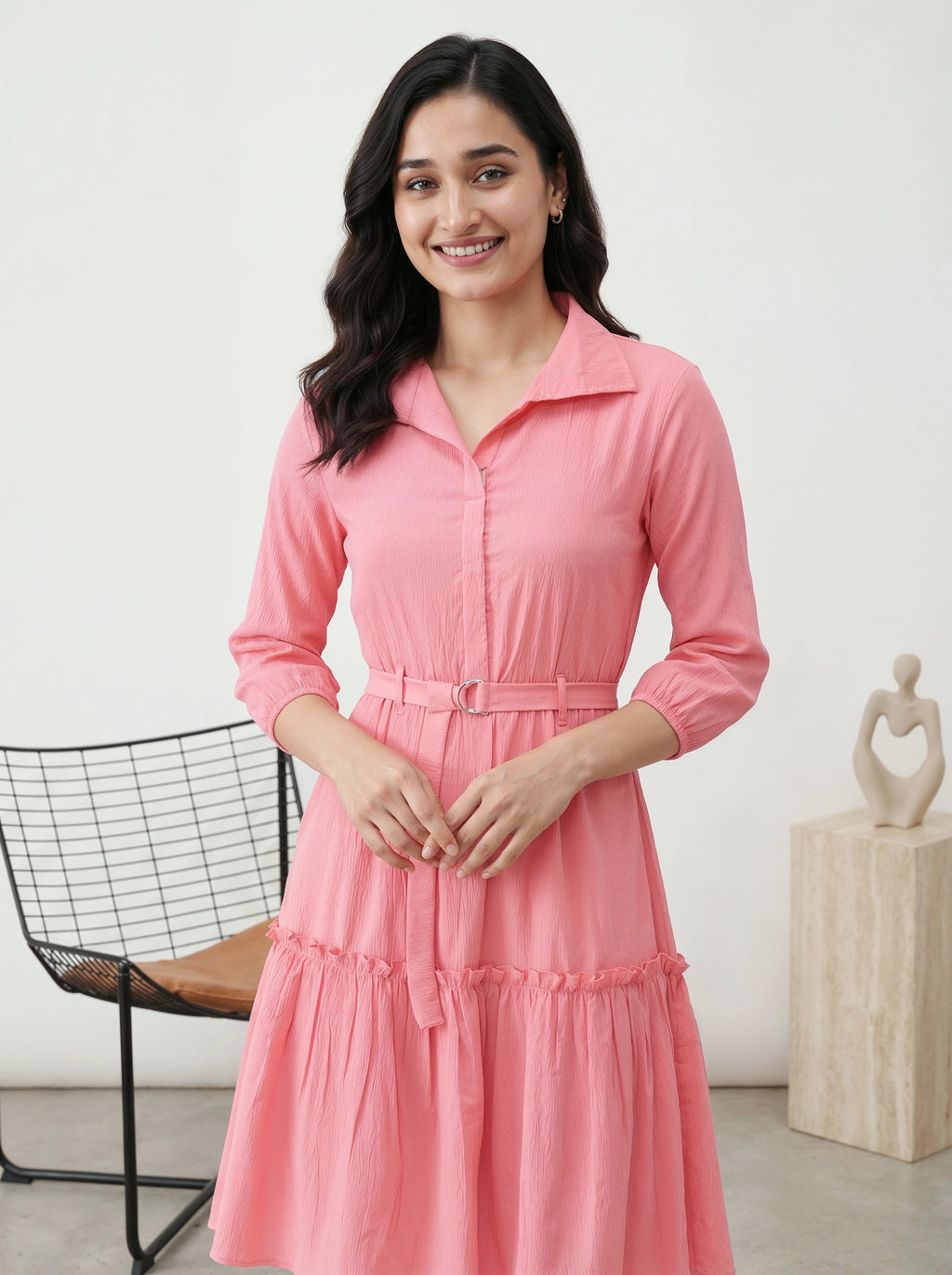 Woman wearing a pink dress standing in a room with a chair and sculpture in the background.