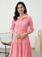 Woman wearing a pink dress standing in a room with a chair and sculpture in the background.