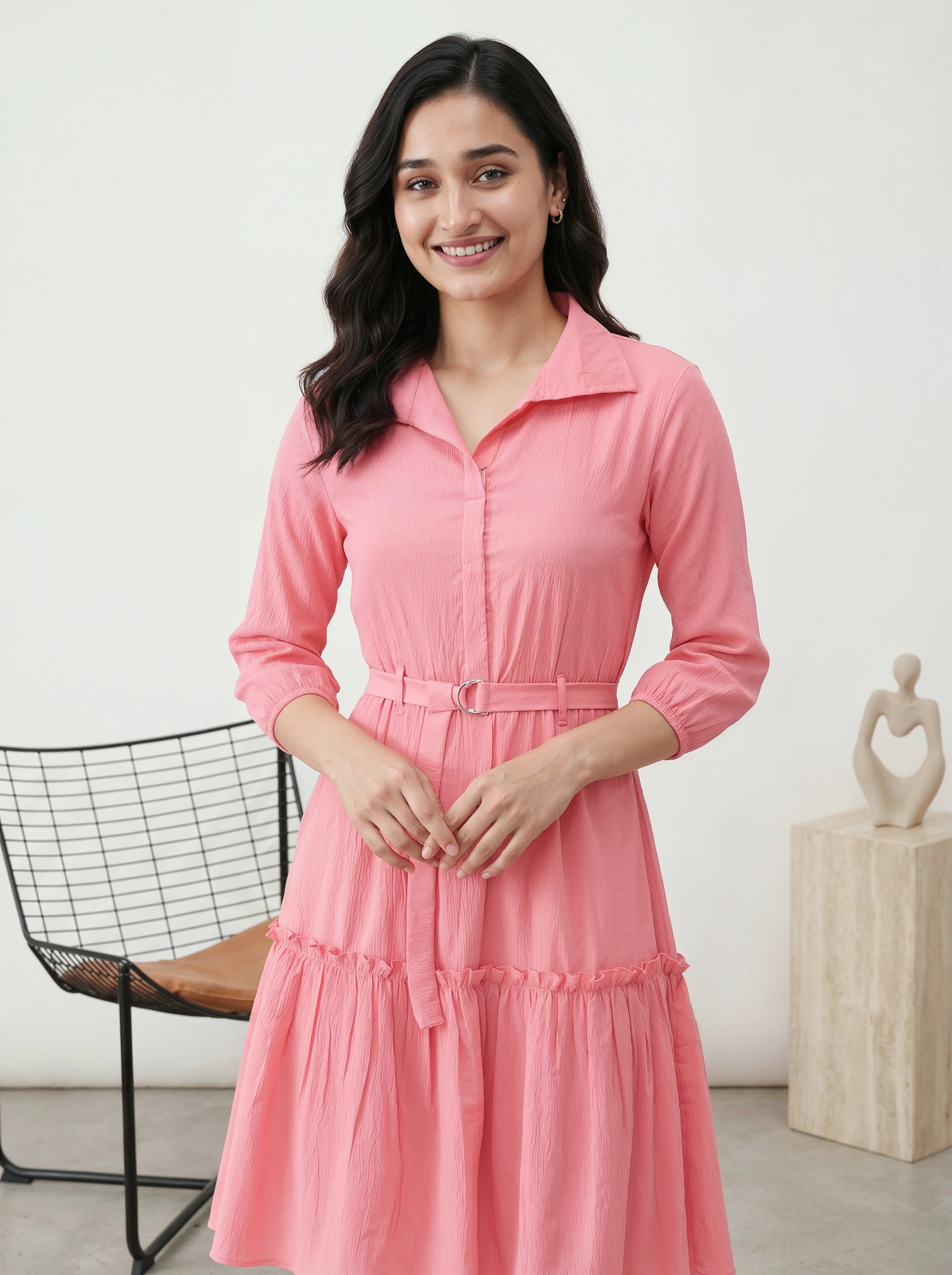 Woman wearing a pink dress standing in a room with a chair and sculpture in the background.