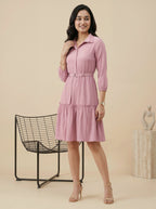 Woman wearing a pink dress standing in a minimalistic room with a chair and decorative object.