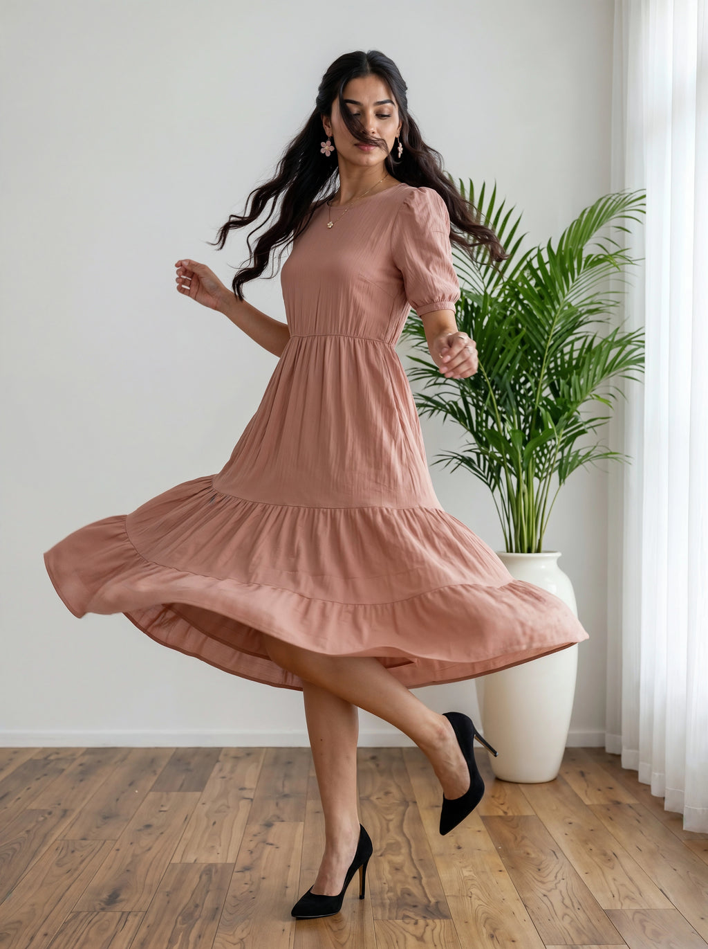 Woman in a peach dress twirling in a room with a plant and white curtain.