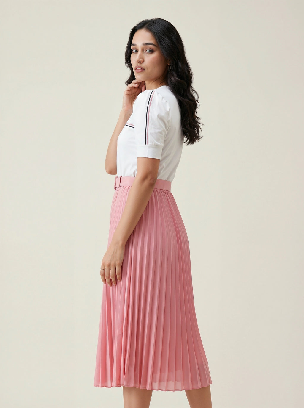 Woman wearing a white top and pink pleated skirt on a plain background