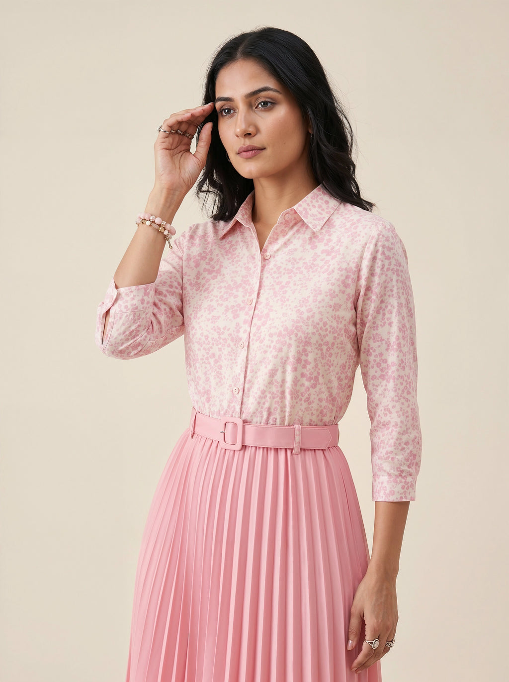 Woman wearing a pink floral blouse and pleated skirt on a beige background