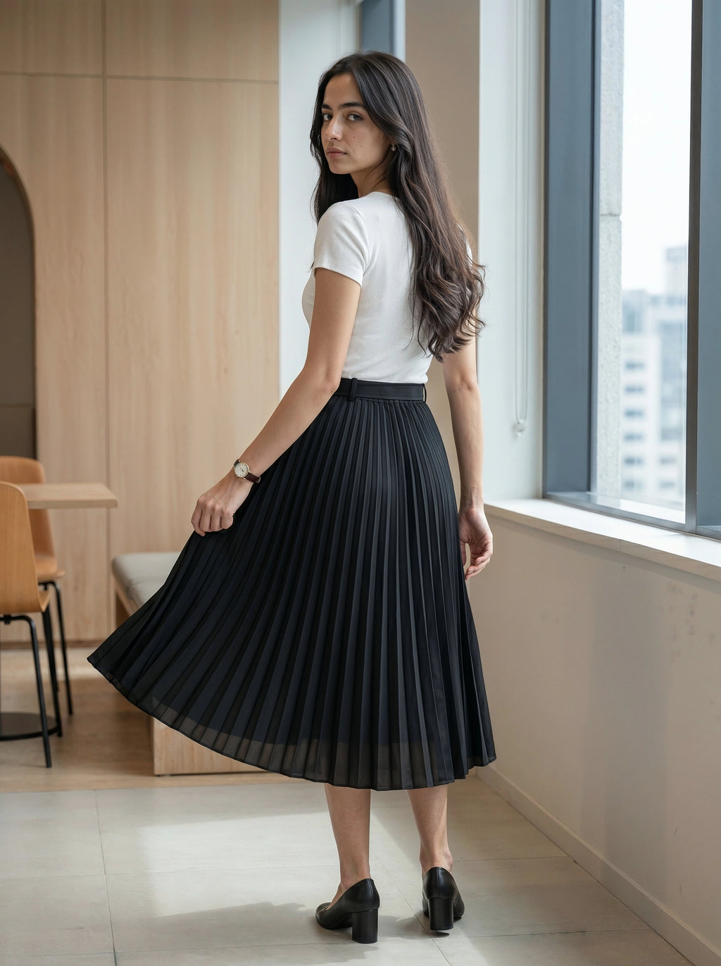 Woman wearing a black pleated skirt and white top in an indoor setting.
