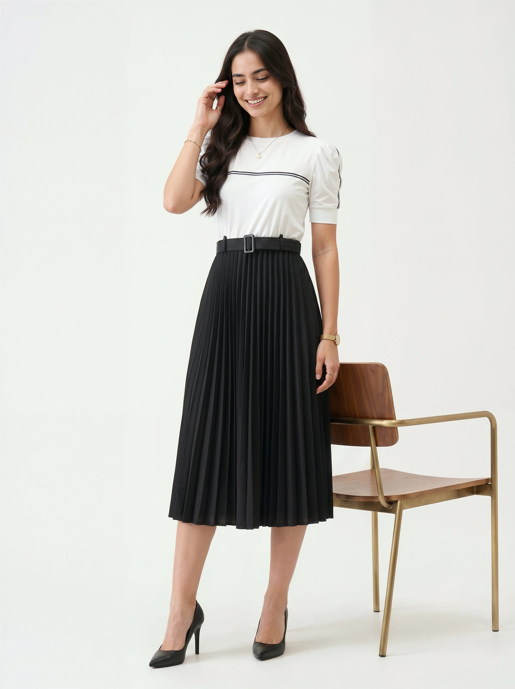 Woman wearing a white blouse and black pleated skirt standing against a white background