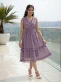 Woman in a purple dress standing on a balcony with a scenic view.