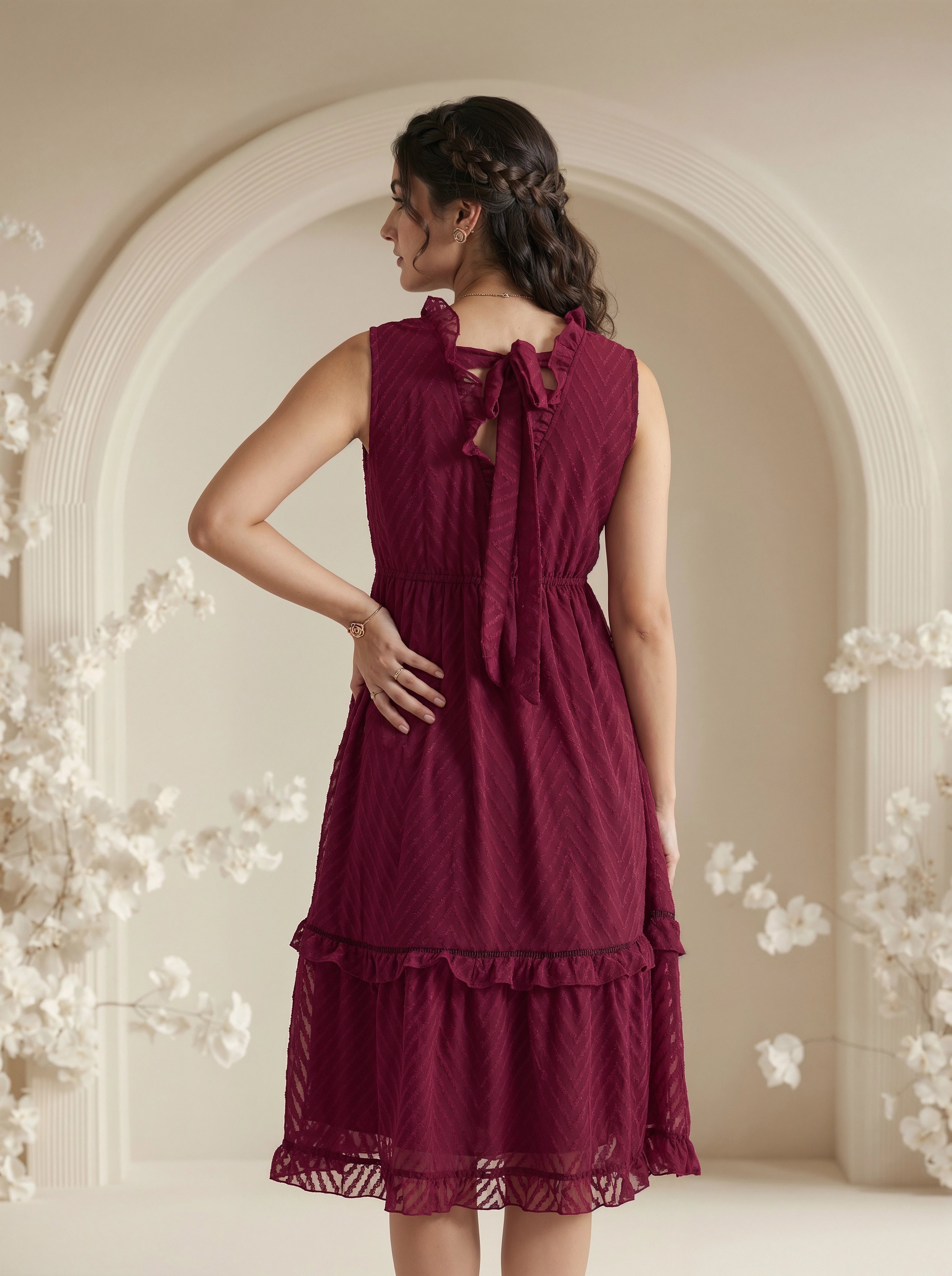 Woman wearing a burgundy dress with floral decorations in an elegant indoor setting.