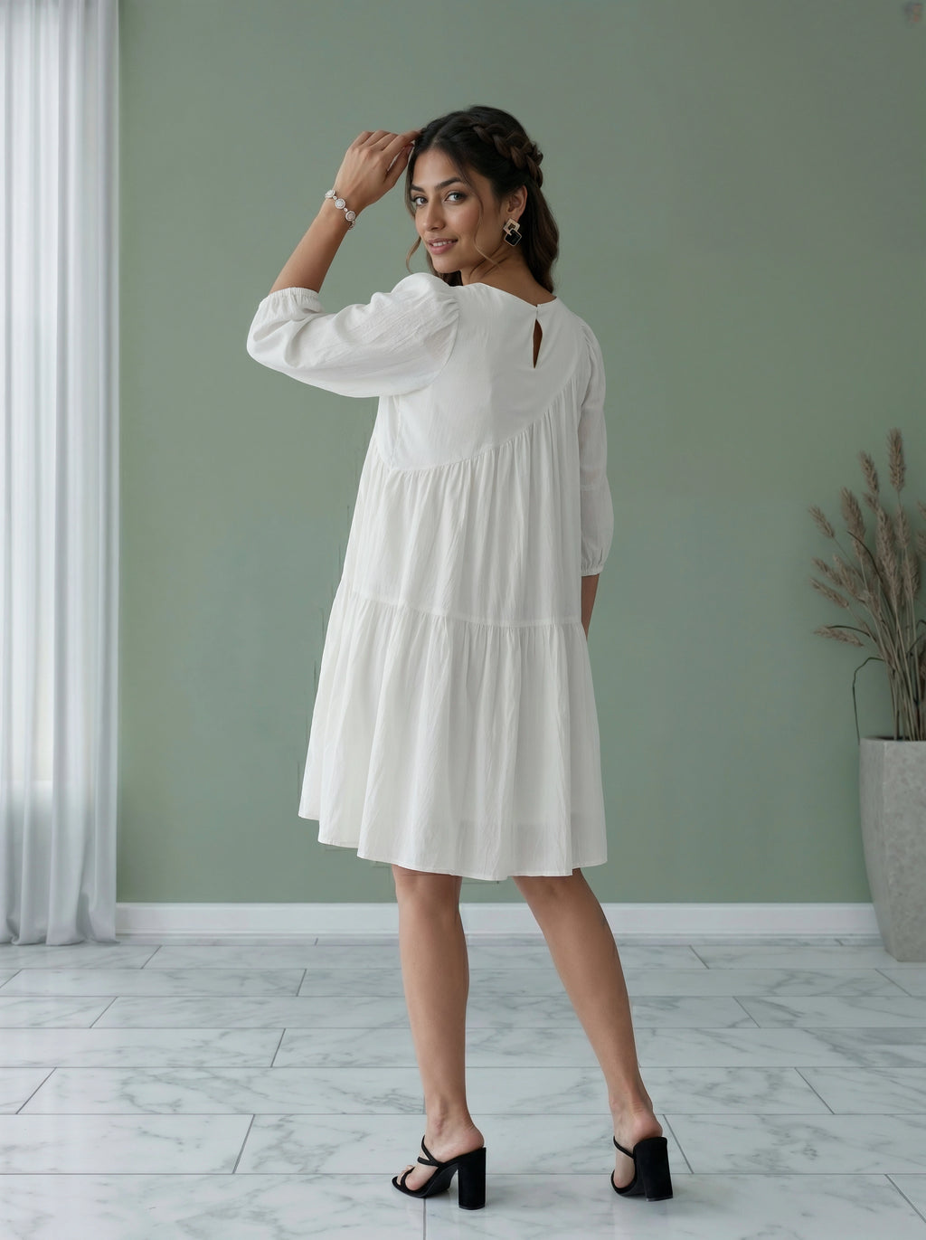 Woman wearing a white dress standing in a room with a green wall and a plant.