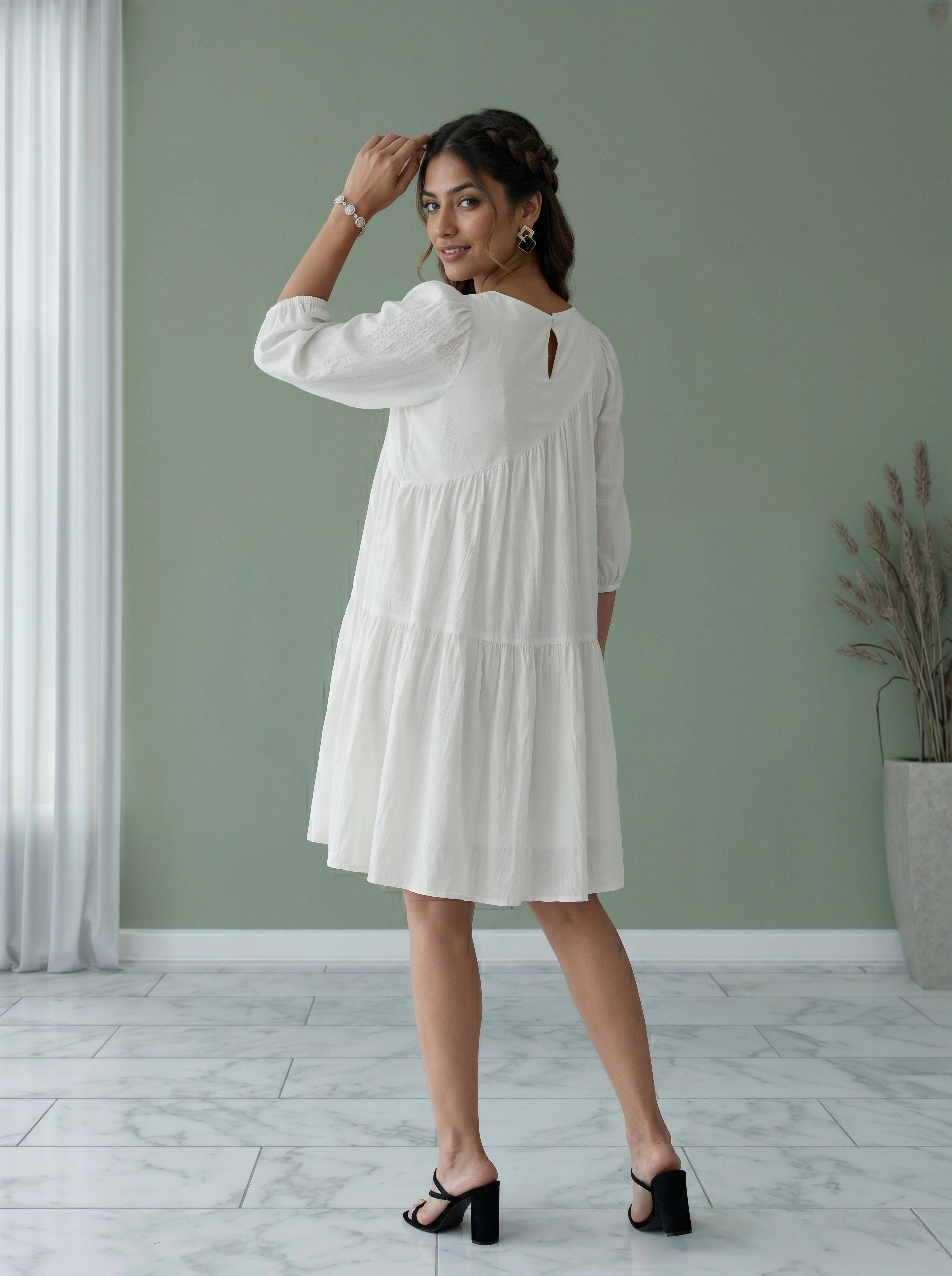 Woman wearing a white dress standing in a room with a green wall and a plant.