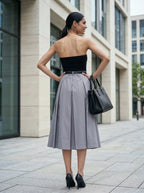 Woman in black top and gray skirt standing on a city street.