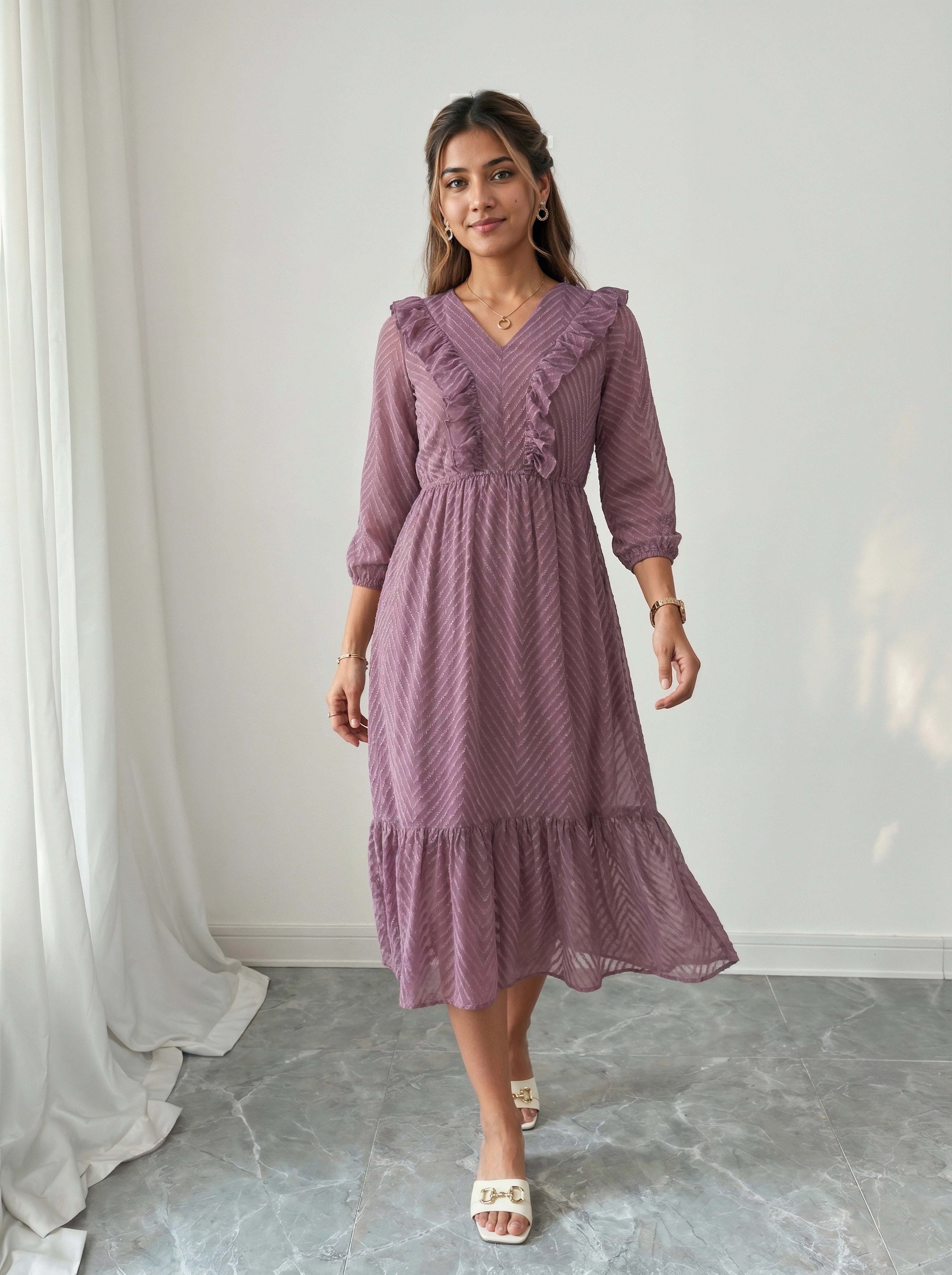 Woman wearing a purple dress standing in a room with white curtains and gray floor.